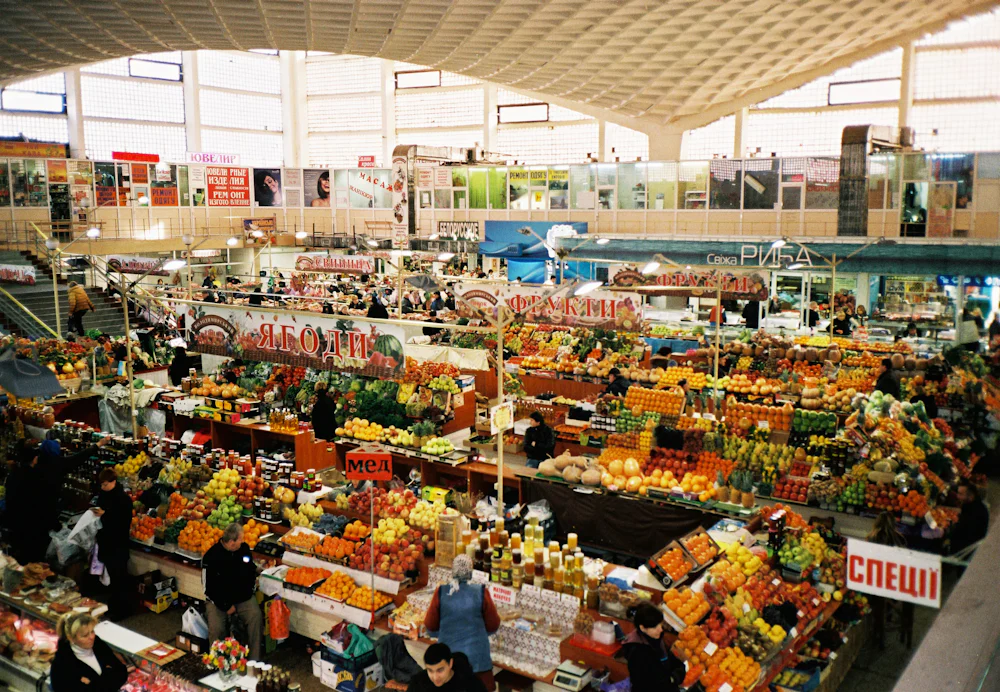 Shoppers and colorful fruit stalls at an indoor market.